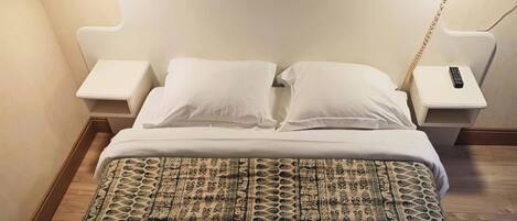 A bed with patterned bedding, a white headboard, bedside tables with lamps, and a wall-mounted phone.