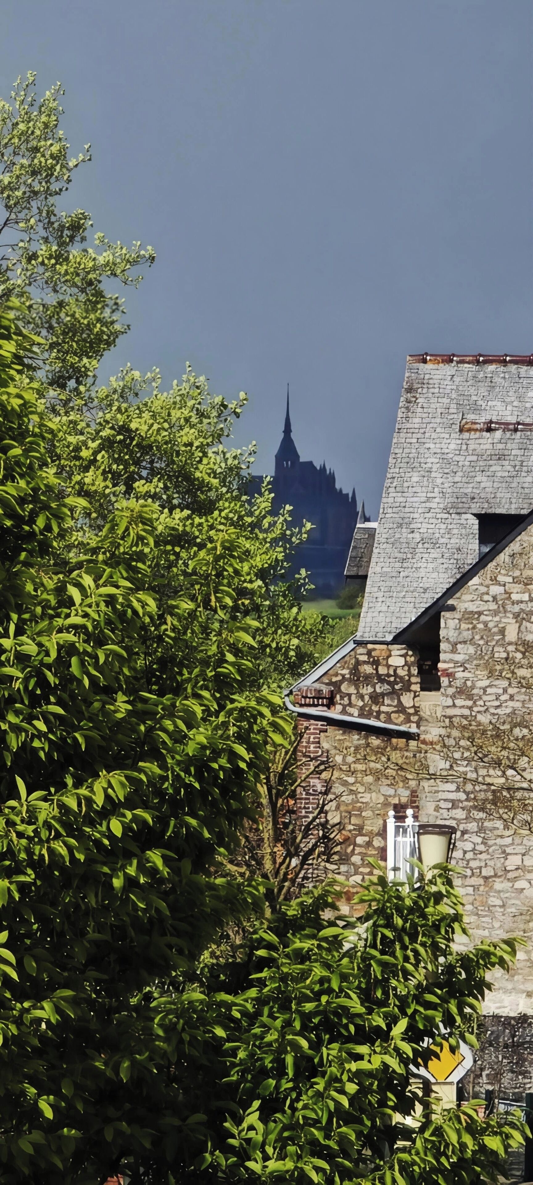 Un edificio con fachada de piedra, una chimenea visible y una ventana con marco blanco.