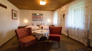 A room with two beds, a table with a vase, and two chairs. - Haus am Waldesrand (Regen)