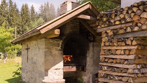 A stone building with a fireplace, a wooden roof, and a stack of firewood. - Haus am Waldesrand (Regen)