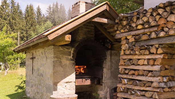 A stone building with a fireplace, a wooden roof, and a stack of firewood. - Haus am Waldesrand (Regen)
