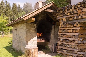 A stone building with a fireplace, a wooden roof, and a stack of firewood. - Haus am Waldesrand (Regen)