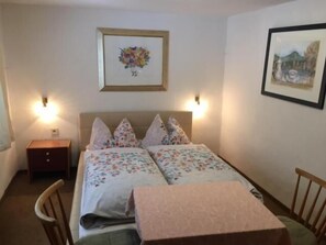 A double bed with floral bedding, a small bedside table, and a chair. - Haus am Waldesrand (Regen)