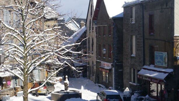 Eine verschneite Straße mit Gebäuden, einer Statue und parkenden Autos.