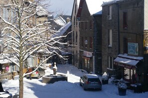 Calle nevada con edificios, una estatua y coches estacionados.