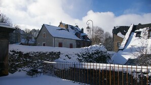 Ein schneebedecktes Haus im ländlichen Stil mit Steinmauer und Metallzaun.