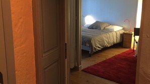Ein schmaler Flur, der zu einem Schlafzimmer führt, mit einem Bett, einem roten Teppich und einem Nachttisch mit Lampe.