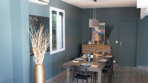 Un comedor con una mesa dispuesta para seis comensales, un jarrón alto con ramas y un cuadro en la pared.
