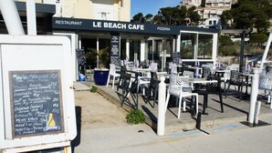 Un área de estar al aire libre con mesas y sillas en LE BEACH CAFE, con un menú y un letrero del restaurante.