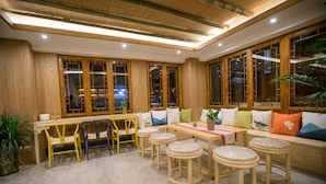 A cozy seating area with wooden furniture, including a sofa and stools, and a table with a red table runner. - Stay in joy Boutique Inn (Qiandongnan)
