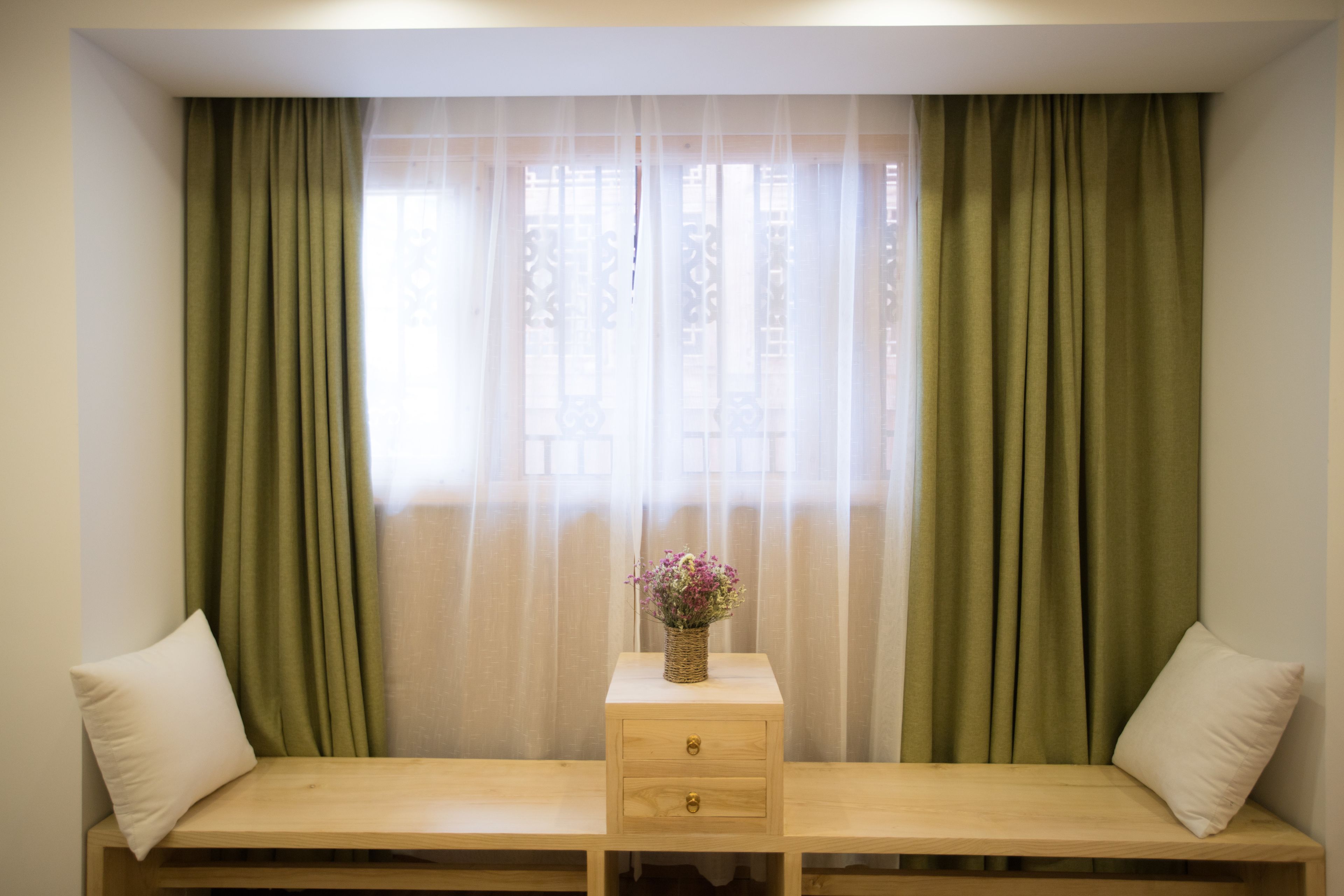 A room with a bed, a small wooden nightstand with a vase of flowers, and green curtains.