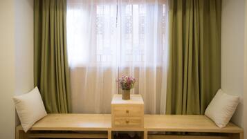 Una habitación con una cama, una mesita de noche de madera con un florero, y cortinas verdes.