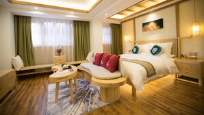 A modern hotel room with a large bed, a curved bench, a small round table, and a bedside table with a lamp. - Stay in joy Boutique Inn (Qiandongnan)
