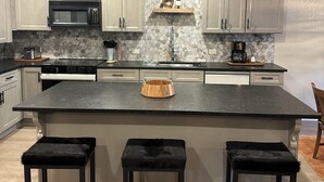 A modern kitchen with a large island, white cabinets, a microwave, and a coffee maker. - Luxury Remodel Downtown Condo Across from Yampa River 
CANNOT BEAT THE LOCATION! (Steamboat Springs)