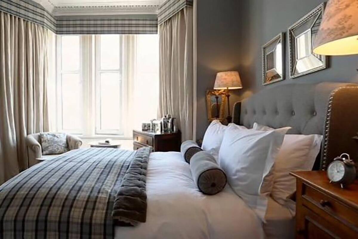 A hotel room with a large bed, a nightstand, a lamp, and a window with curtains.