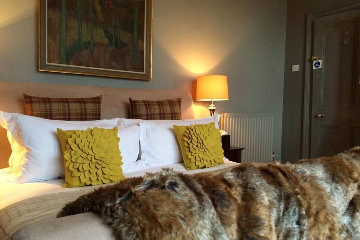 A hotel room with a bed, a painting on the wall, a lamp, and a door.