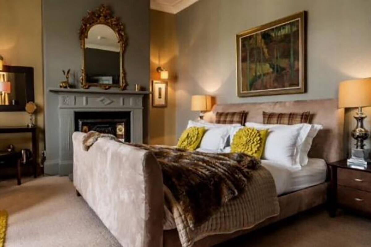 A bedroom with a large bed, a fireplace, a mirror, and two bedside lamps.
