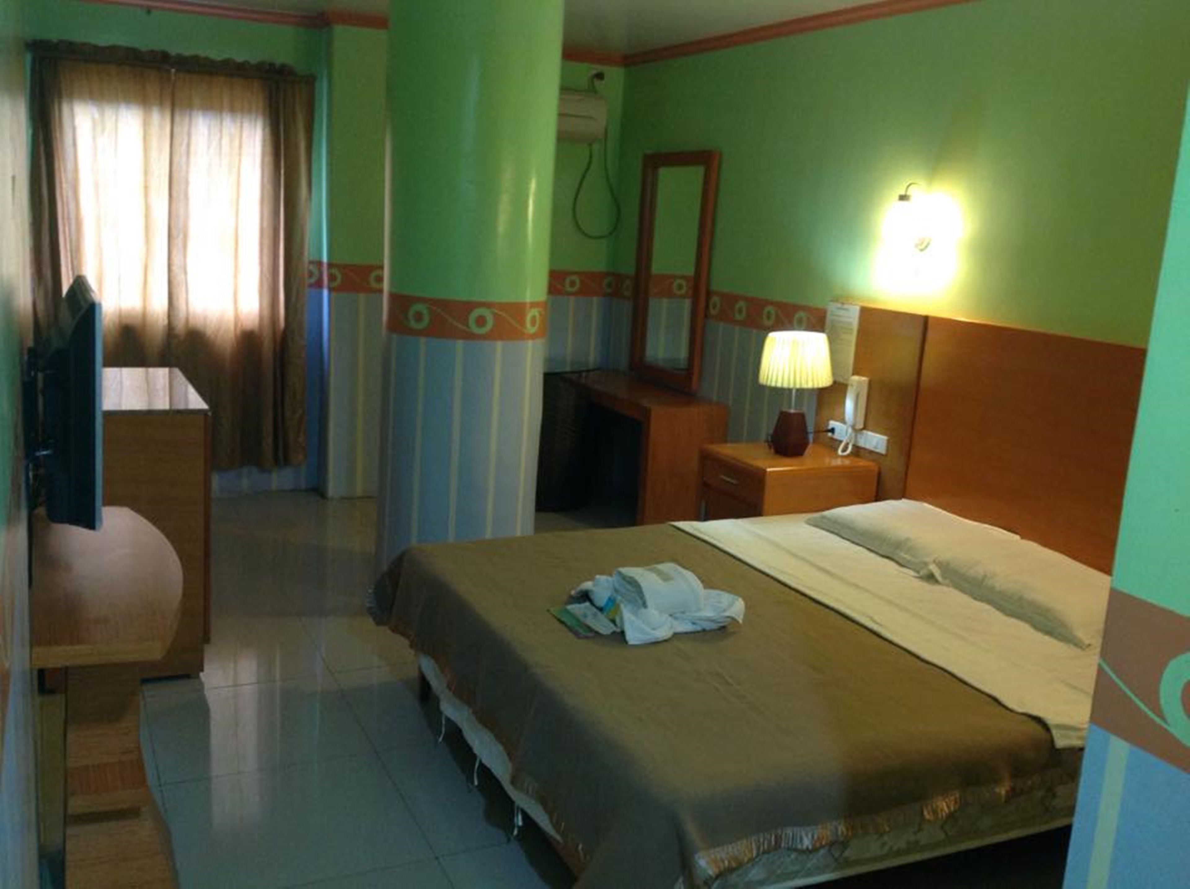Una habitación de hotel con cama, escritorio, silla, espejo y lámpara.