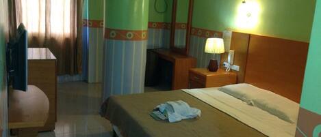 Una habitación de hotel con cama, escritorio, silla, espejo y lámpara.
