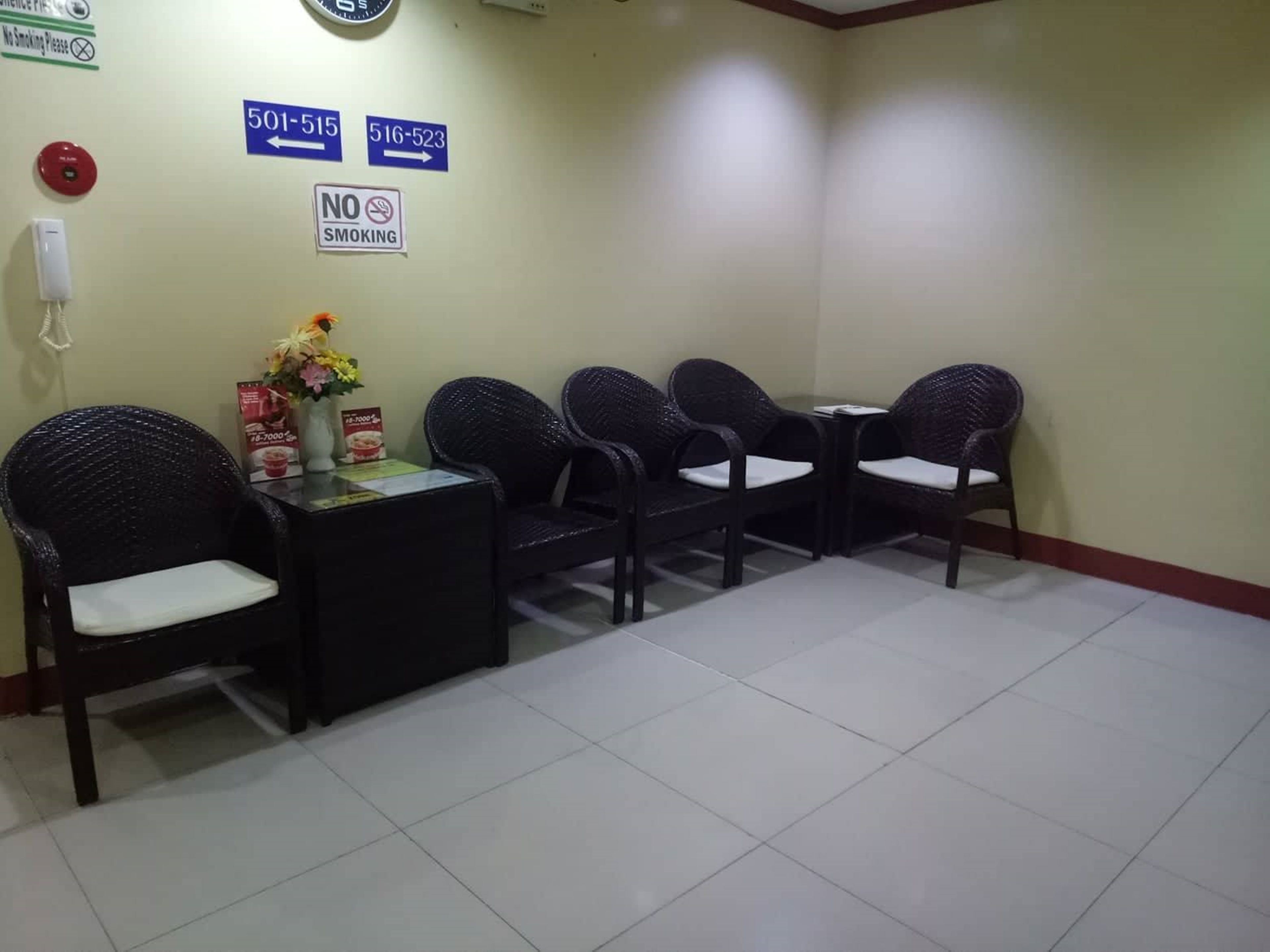 A waiting area with chairs and tables, a no-smoking sign, and emergency contact numbers on the wall.