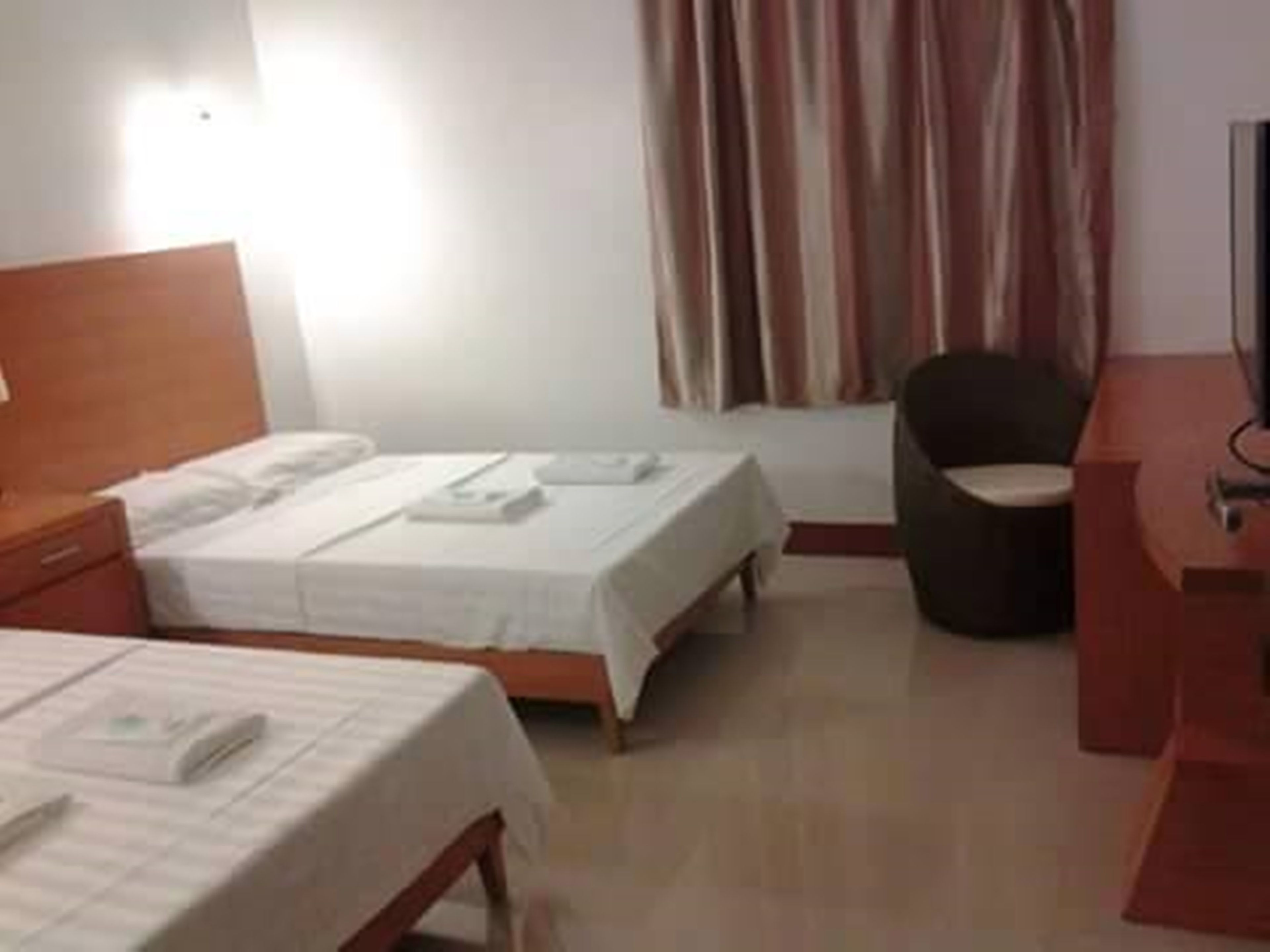 A hotel room with two single beds, a wooden nightstand, a desk, and a chair.