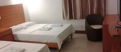 A hotel room with two single beds, a wooden nightstand, a desk, and a chair.