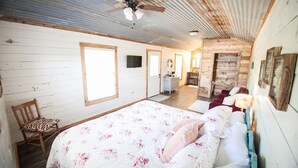 Un dormitorio con cama, paredes de madera, ventilador de techo y una pequeña zona de escritorio.