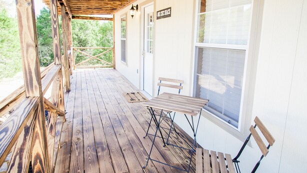 Una terraza de madera con una mesa y sillas, un letrero que dice “The Cabin Shack”, y vistas a árboles a través de las ventanas.