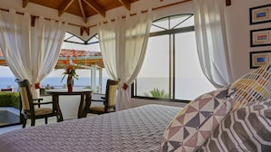 Ein Schlafzimmer mit einem großen Bett, Meerblick und einem Tisch mit Stühlen draußen.