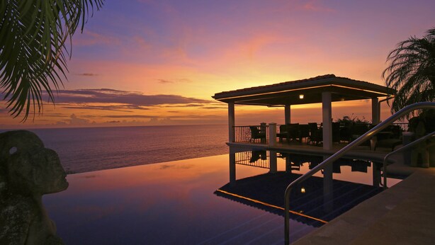 Ein Infinity-Pool mit überdachter Sitzgelegenheit mit Blick auf den Ozean bei Sonnenuntergang.