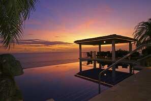 An infinity pool with a covered seating area overlooking the ocean at sunset. - Luxury Oceanview Villa with Private Chef, Infinity Pool, & Staff (Puerto Carrillo)
