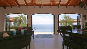Ein geräumiges Zimmer mit Meerblick, ausgestattet mit einer Essecke mit Tisch und Stühlen, einem Sofa und einem dekorativen Teppich.