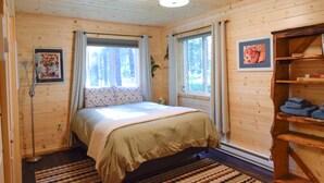 A wooden cabin bedroom with a bed, two windows with curtains, a floor lamp, and a shelf with towels. - Beachfront property located on Resurrection Bay! (Lowell Point)