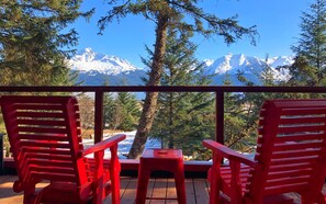 Une terrasse avec des chaises rouges et une table, offrant une vue sur une chaîne de montagnes enneigées.