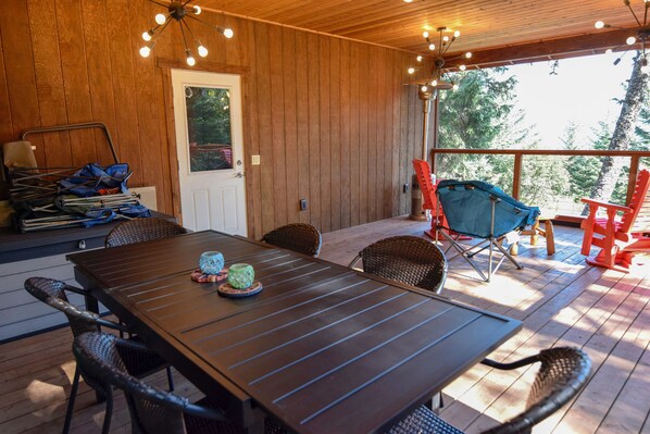 Une terrasse en bois avec une table et des chaises, une porte et une vue sur les arbres.