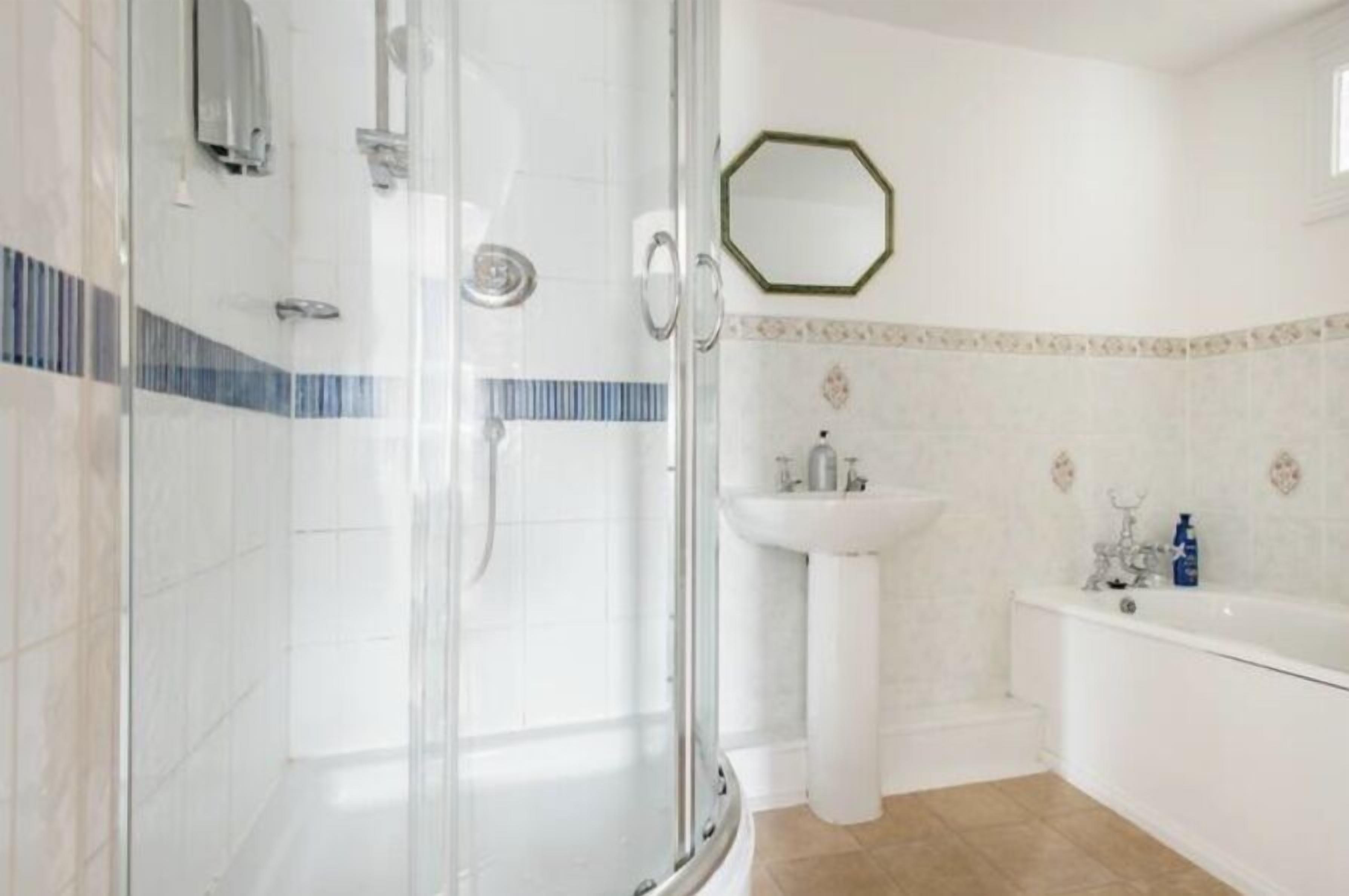 A bathroom with a glass shower enclosure, a pedestal sink, and a bathtub.
