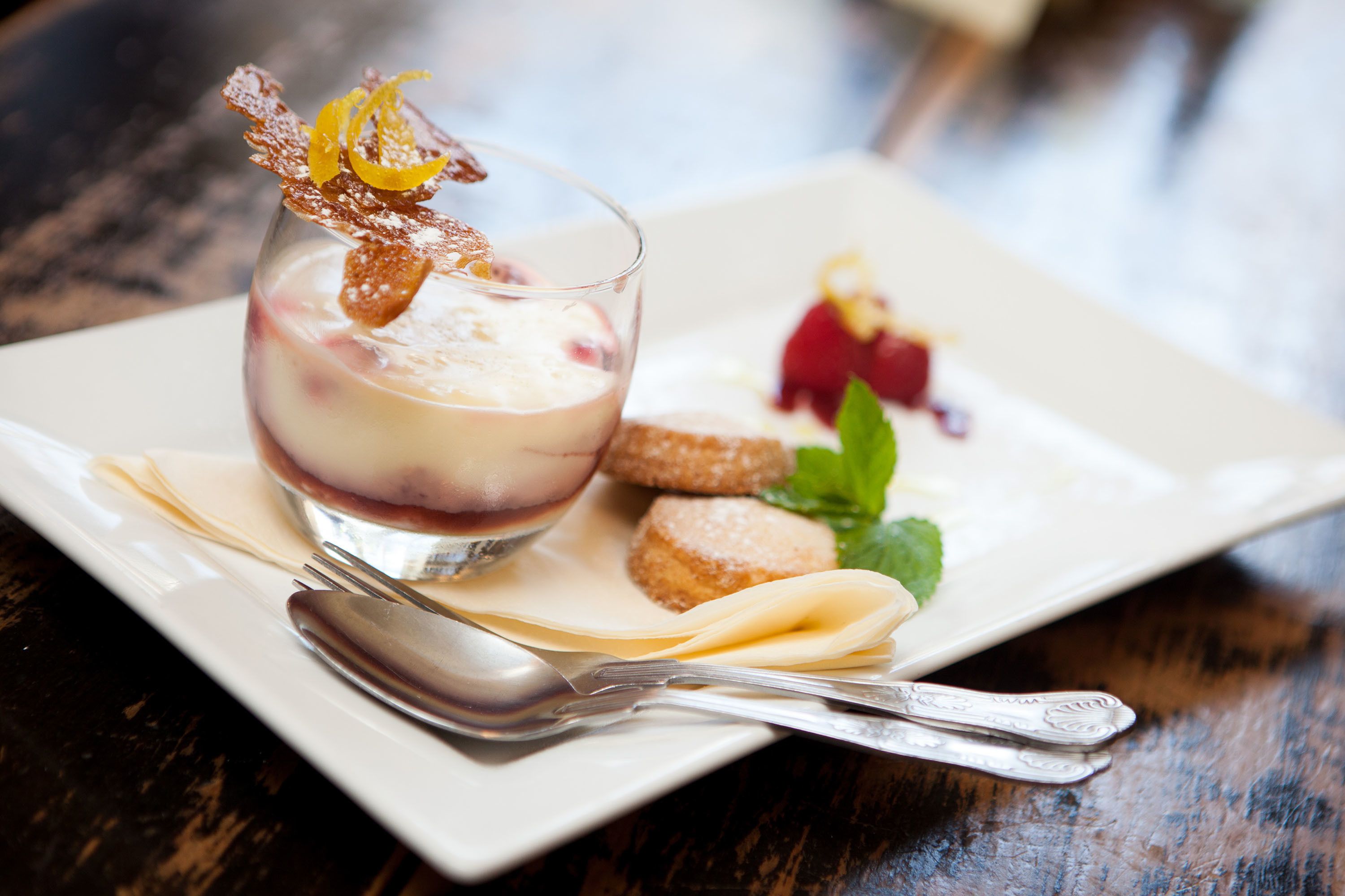 Un postre con un recipiente de vidrio, una cuchara y un plato sobre una mesa de madera.