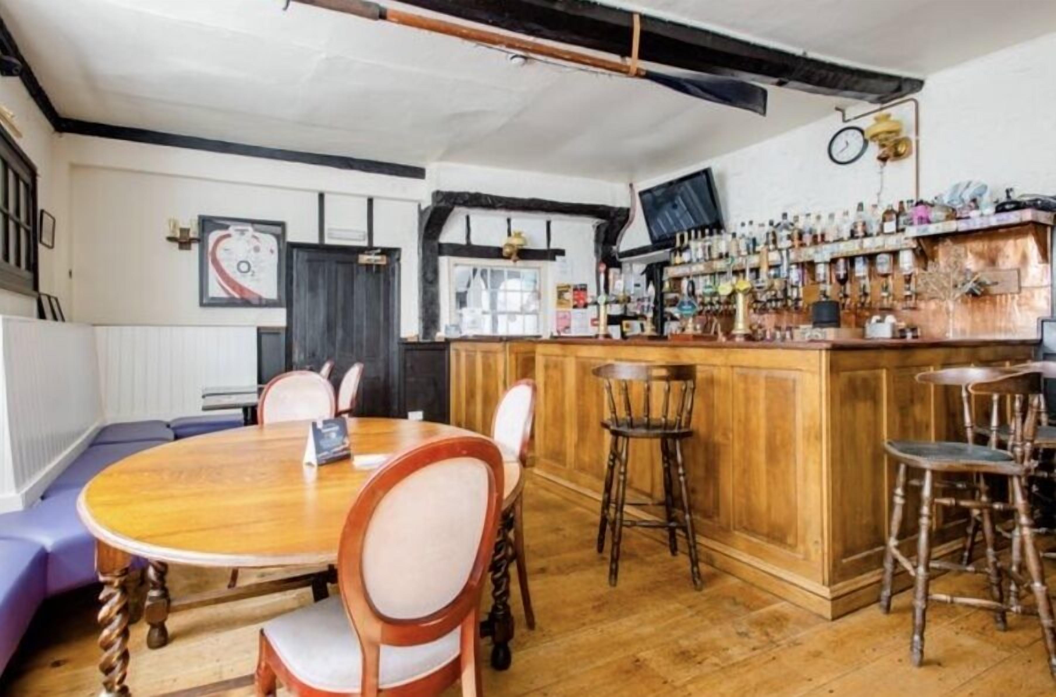 Un área de bar con muebles de madera, una mesa redonda de madera y una barra con taburetes.