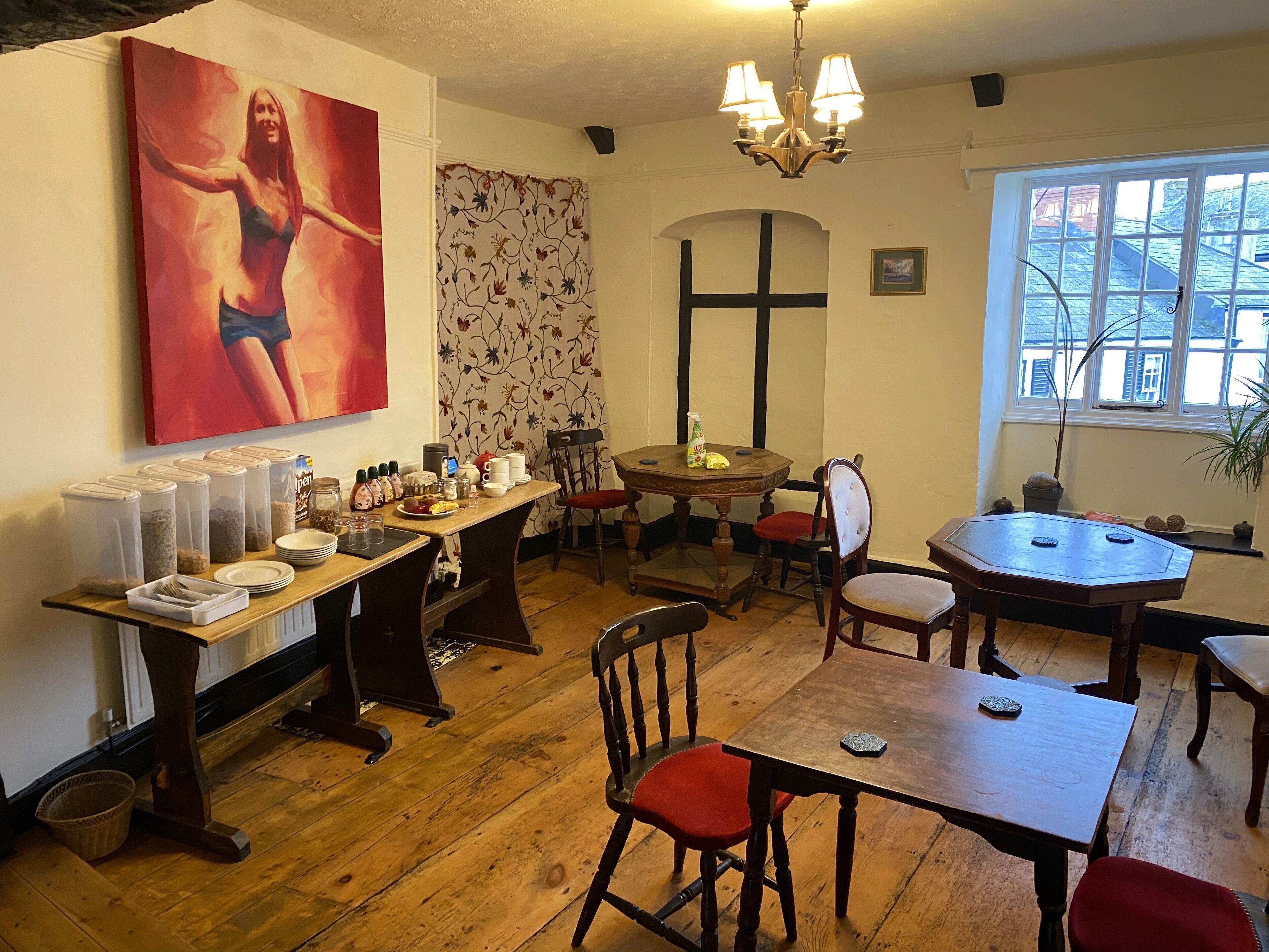 Un espace repas avec des tables et des chaises en bois, un lustre et un tableau accroché au mur.