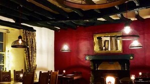 A cozy restaurant interior with wooden tables and chairs, hanging pendant lights, and a fireplace. - The Tree Inn (Bude)