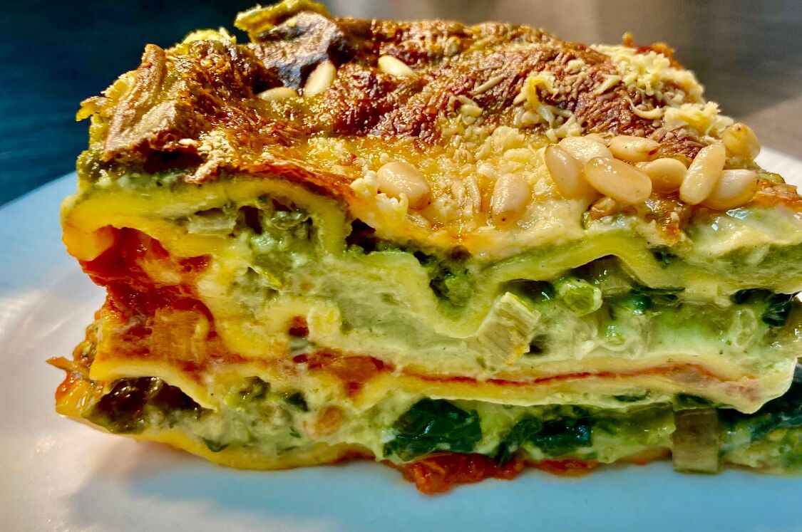 A slice of layered vegetable lasagna with cheese and nuts on top.