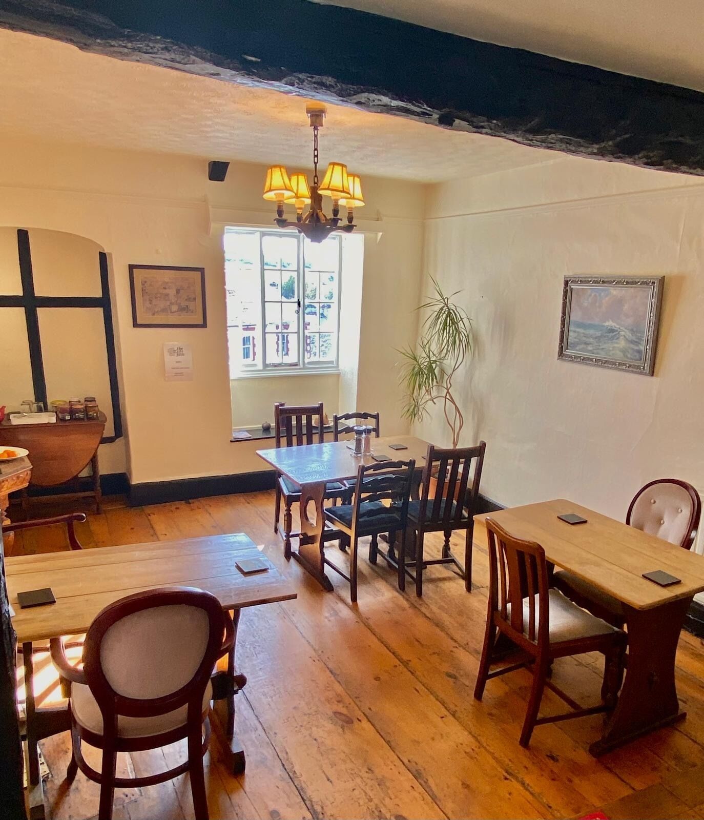 A dining area with wooden tables and chairs, a chandelier, and a window with a view of buildings.