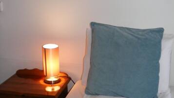 A single bed with a blue pillow and a bedside table with a lamp.