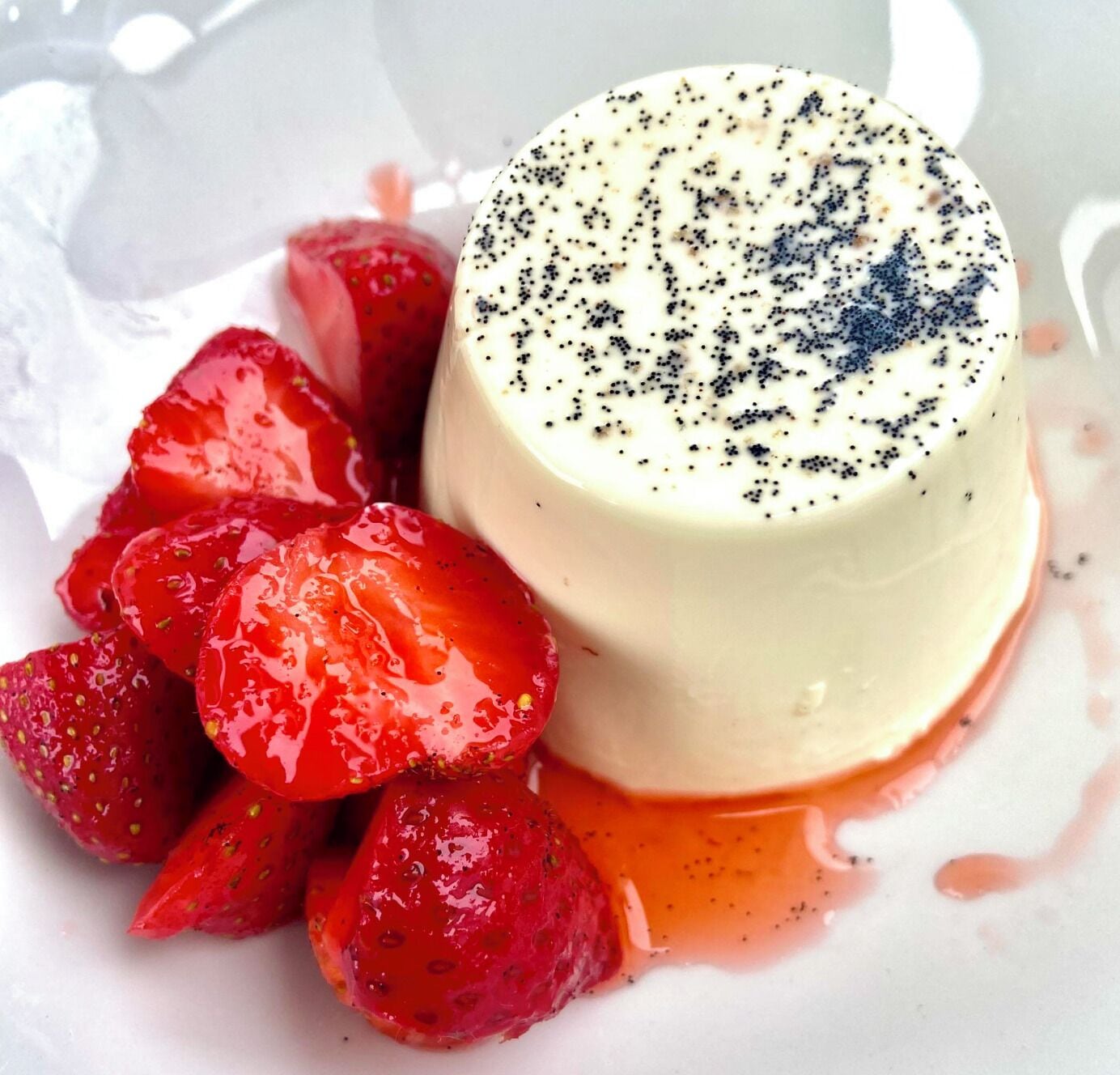 Une panna cotta, dessert à base de crème, servie avec des fraises et nappée d’une sauce.