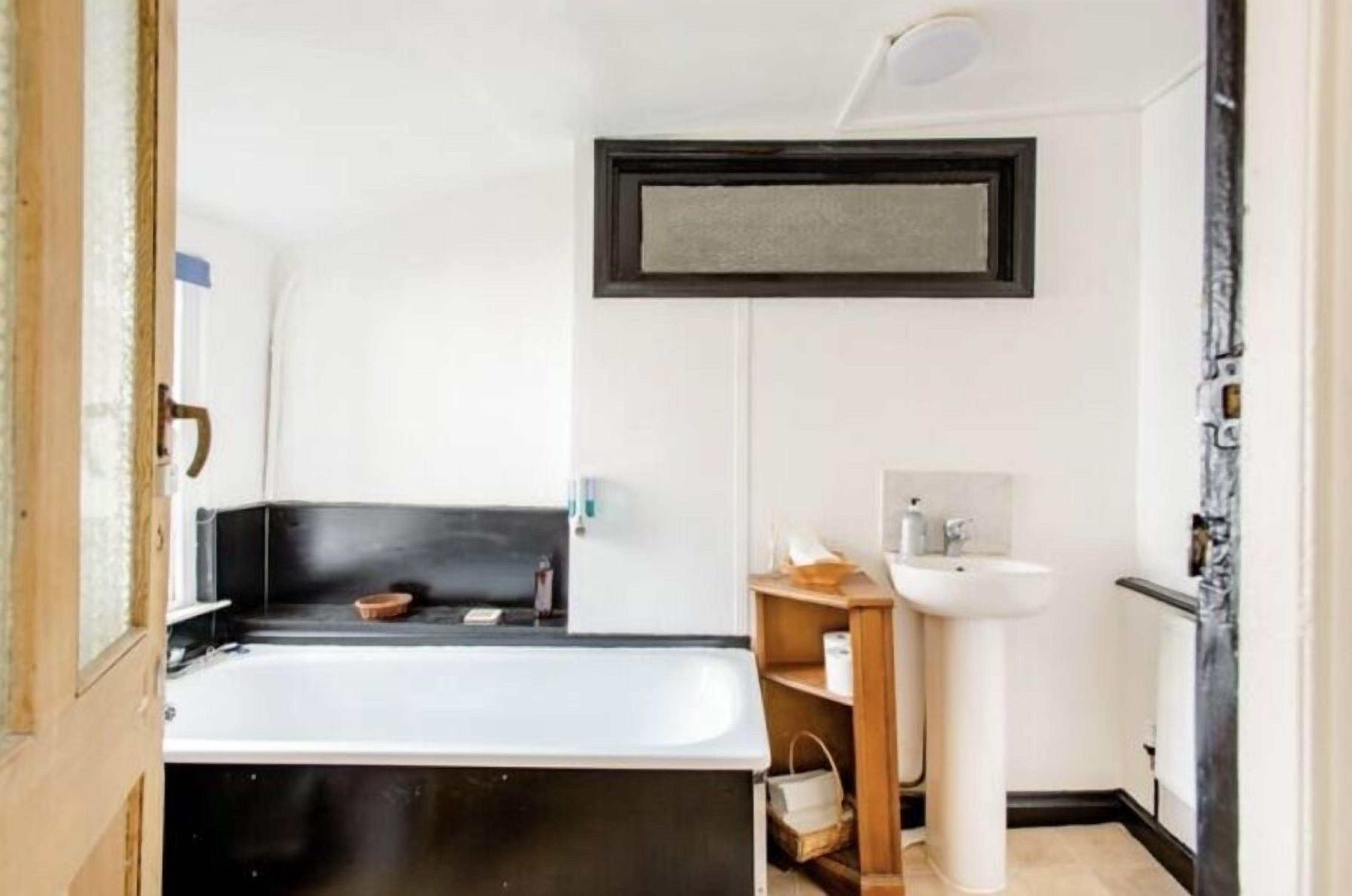 A modern bathroom with a black bathtub, a white sink, and a wooden shelf.