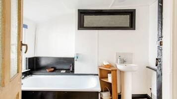 A modern bathroom with a black bathtub, a white sink, and a wooden shelf.