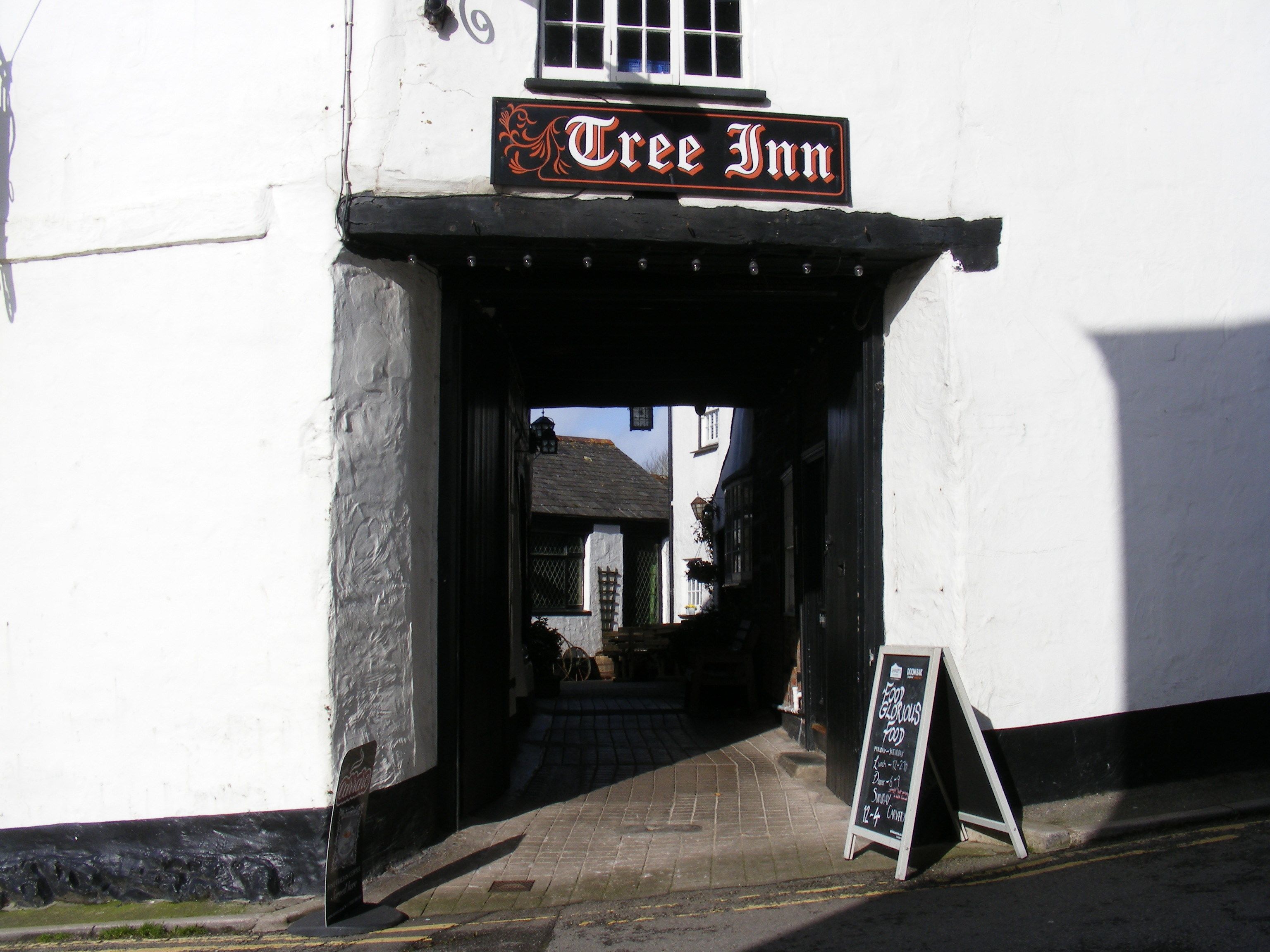 La entrada a Tree Inn, un edificio blanco tradicional con un cartel negro sobre la puerta.