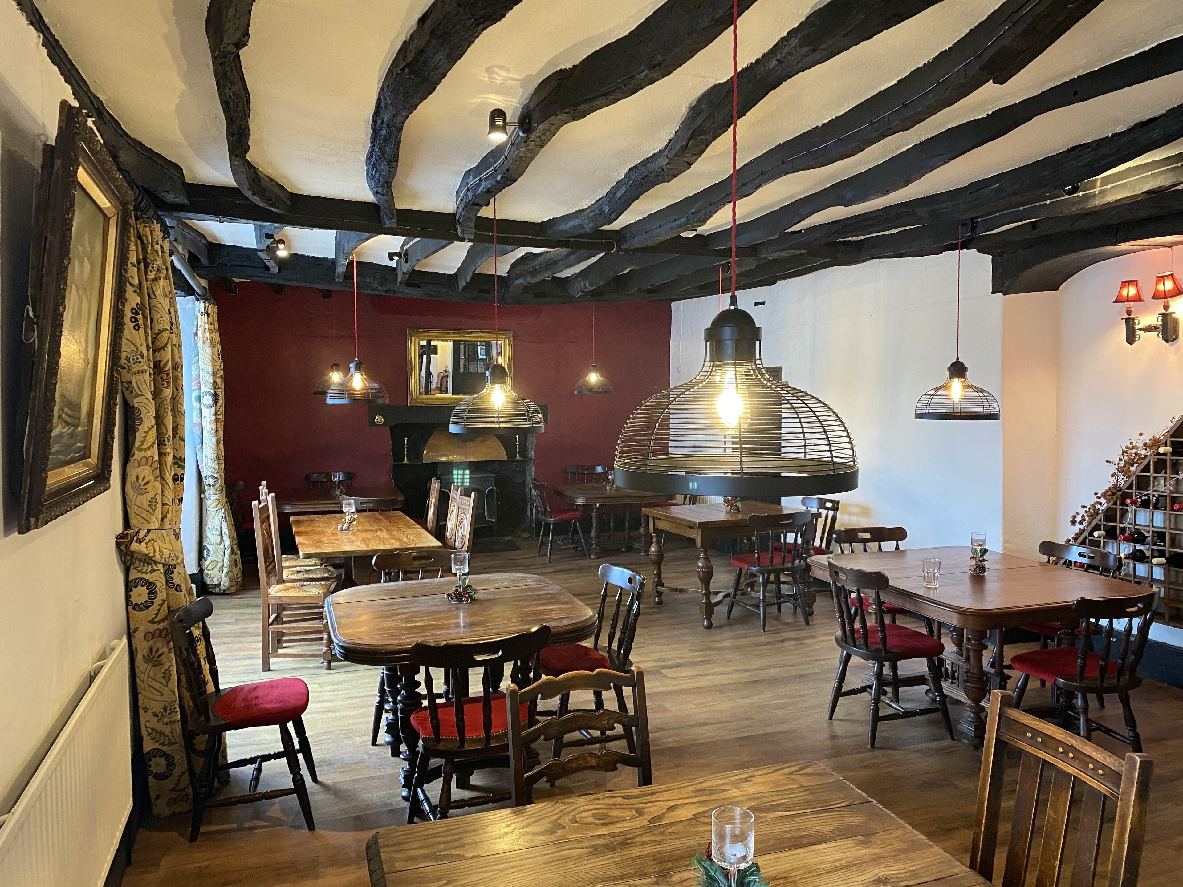 A restaurant with wooden tables and chairs, a fireplace, and hanging pendant lights.