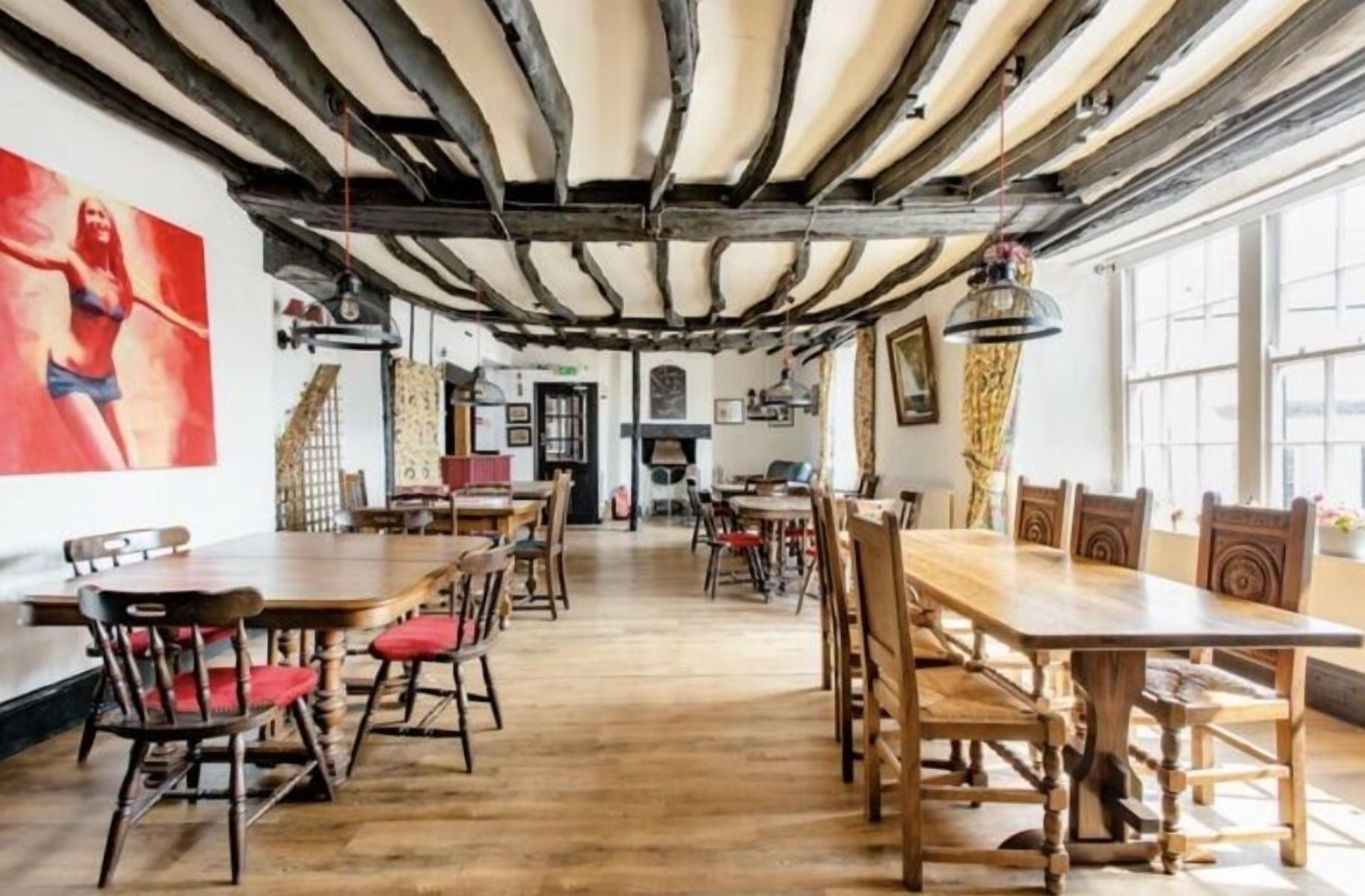 A dining area with wooden tables and chairs, a high ceiling with exposed beams, and large windows allowing natural light.
