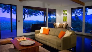 A modern living room with a sofa, coffee table, and large windows offering a view of trees and hills. - Private Wine Country Estate with Panoramic Views, Tennis Court - TOT Cert 450N (Kenwood)